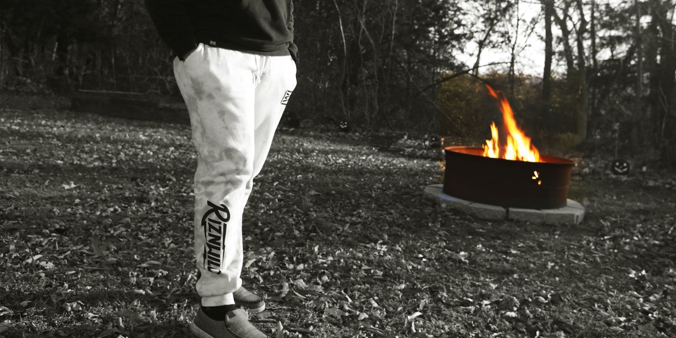 Woman wearing RIZNWILD sweatpants outdoors near a campfire