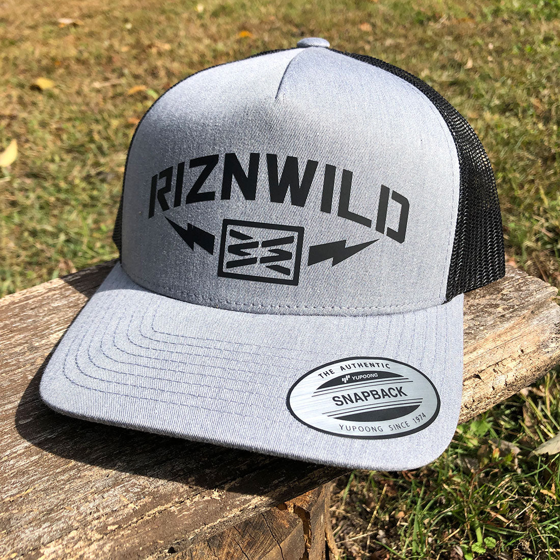RIZNWILD “Storm” heather grey and black trucker hat with bold lightning bolt logo. Snapback mesh cap built for everyday streetwear and outdoor lifestyle.