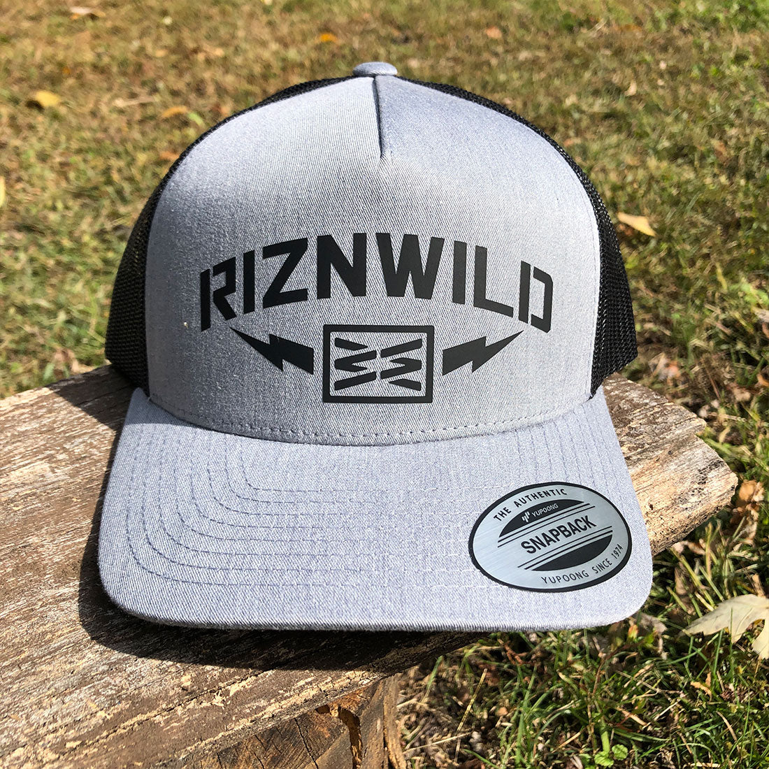 RIZNWILD “Storm” heather grey and black trucker hat with bold lightning bolt logo. Snapback mesh cap built for everyday streetwear and outdoor lifestyle.