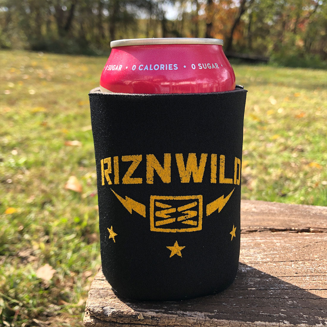 Front view of black and gold RIZNWILD drink cooler sleeve in natural outdoor setting.