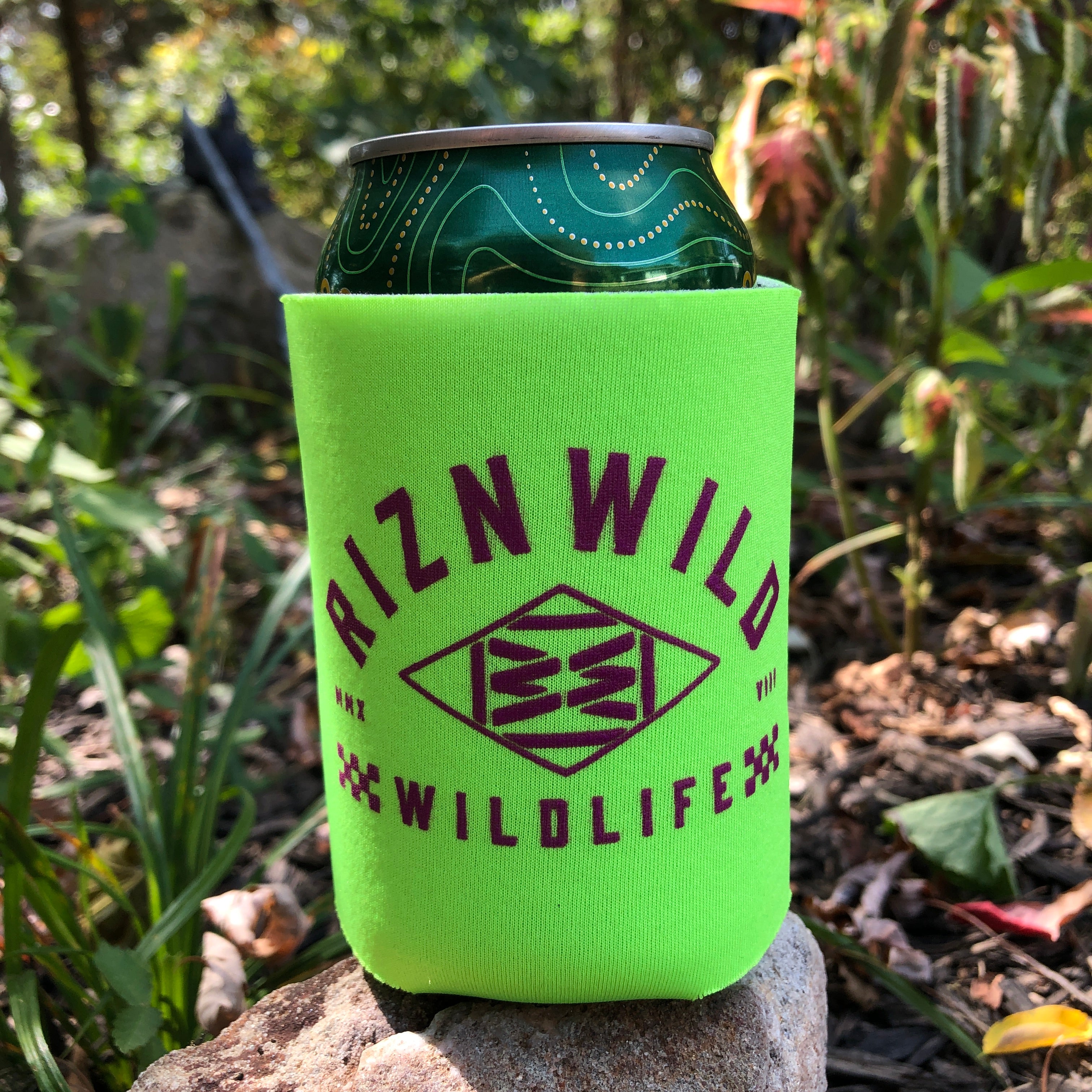 Neon green RIZNWILD can koozie with purple Wildlife logo sitting on a rock outdoors