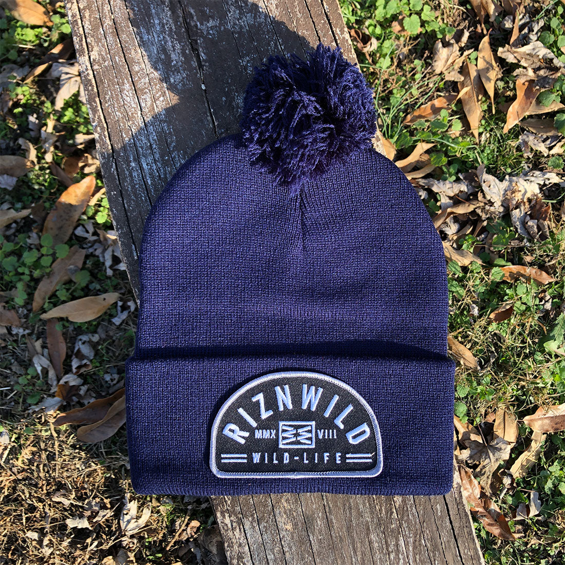 Navy blue pom pom beanie with embroidered RIZNWILD Wild Life patch outdoors