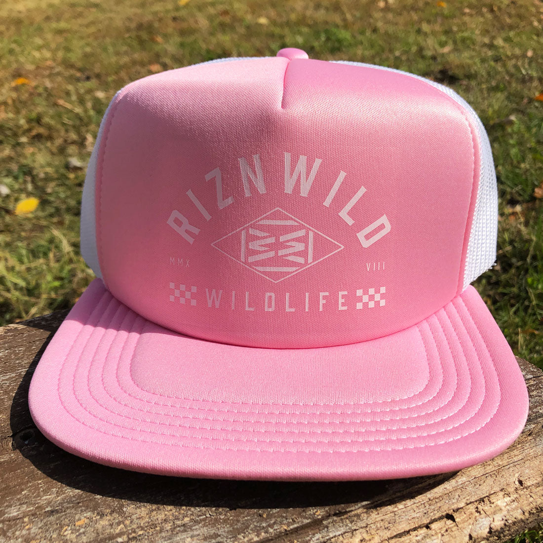 Light pink RIZNWILD wildlife logo foam trucker cap with white mesh back, photographed in natural sunlight