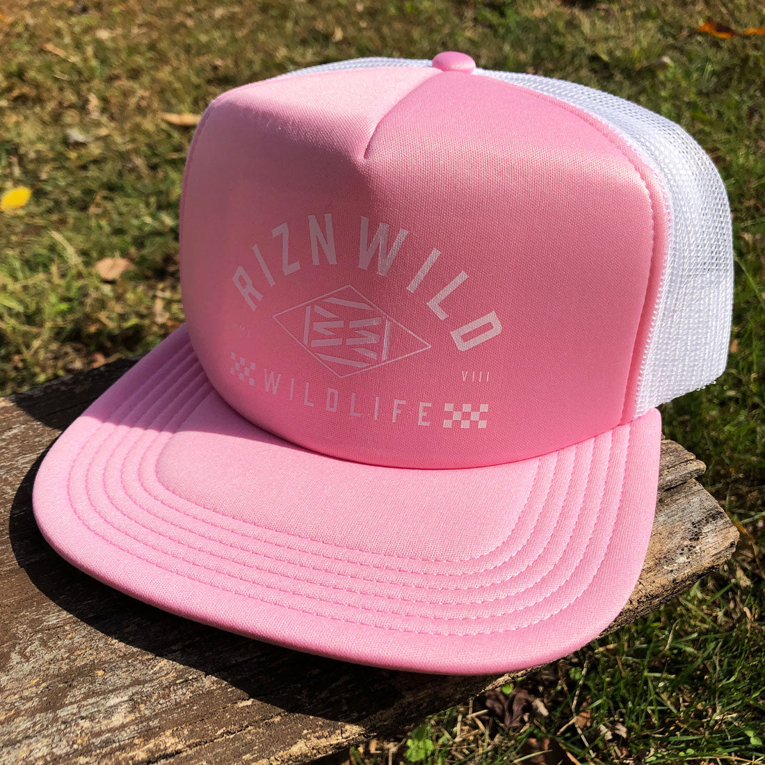 RIZNWILD pink and white trucker hat resting outdoors, showcasing the adventurous wildlife-inspired streetwear style