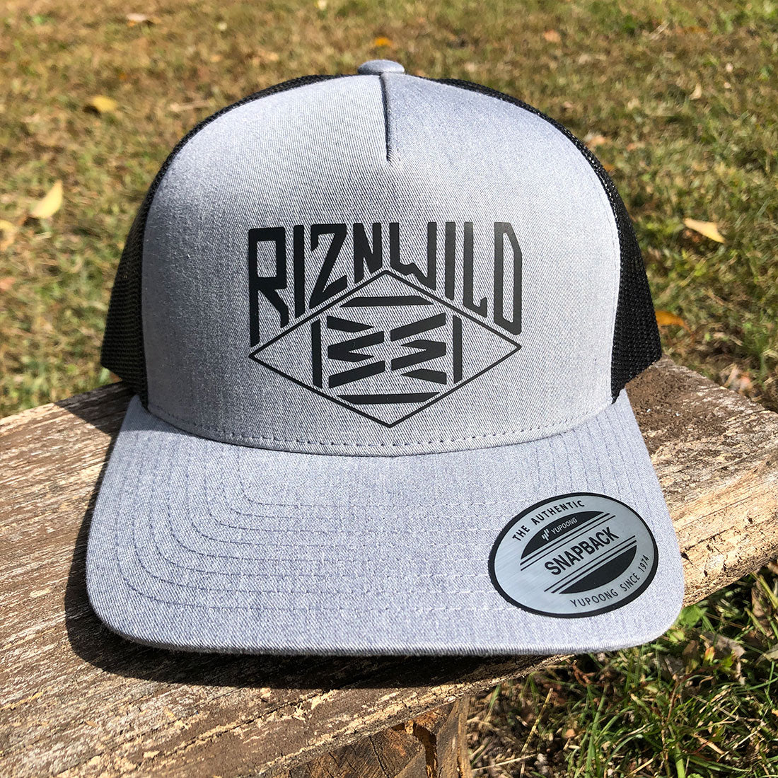 RIZNWILD heather grey and black snapback trucker hat with bold front logo, mesh back, and flat brim.