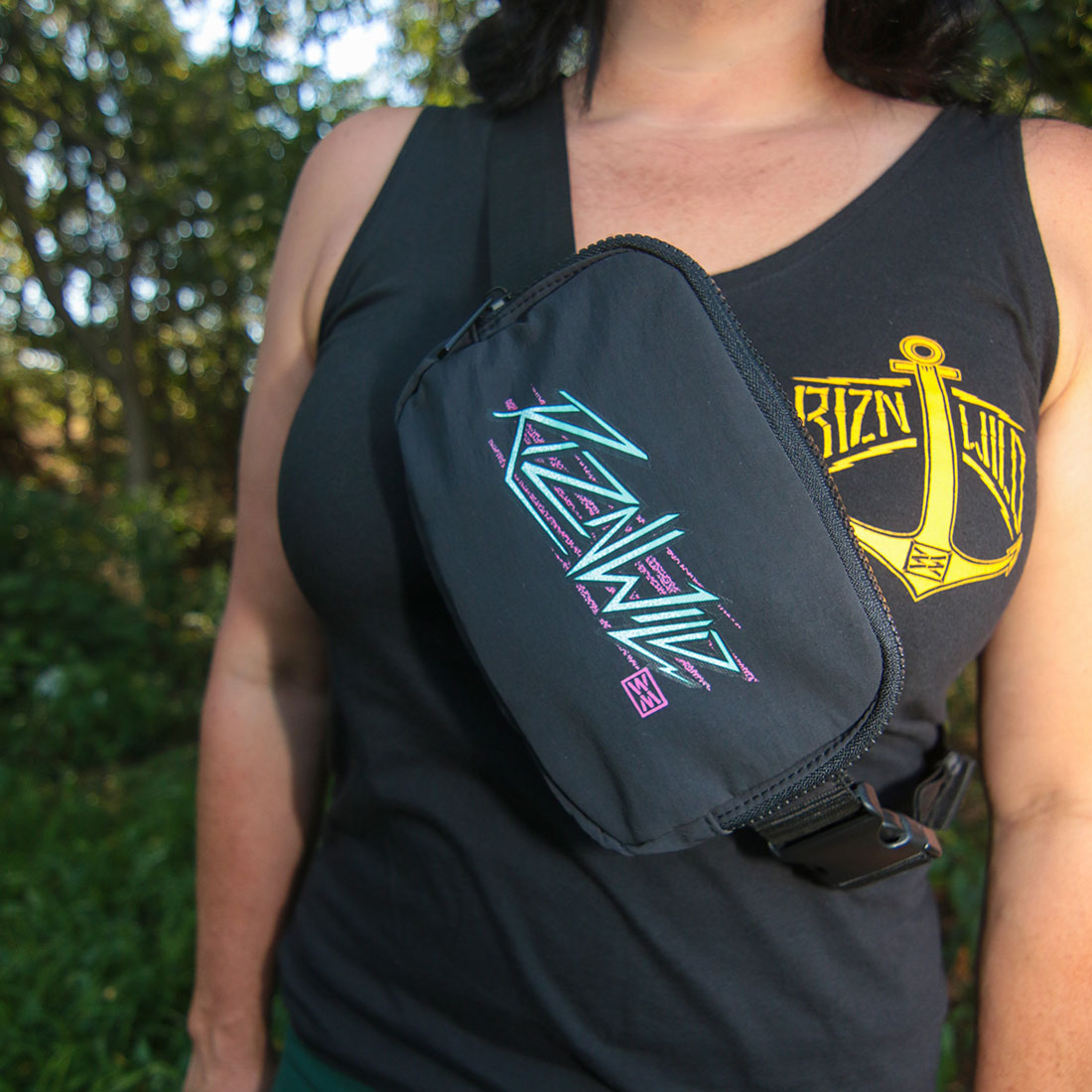 A black crossbody fanny pack with a colorful 'RIZNWILD' graphic, worn by a person in a black tank top outdoors.