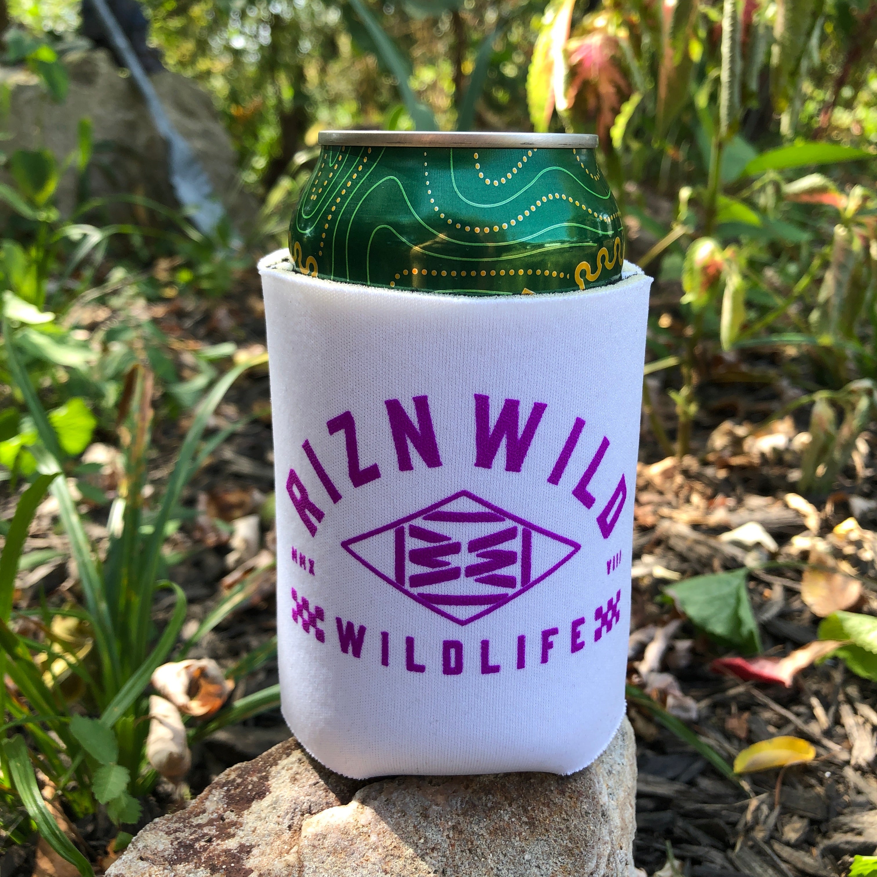 RIZNWILD white drink koozie with bold purple print in a natural outdoor setting